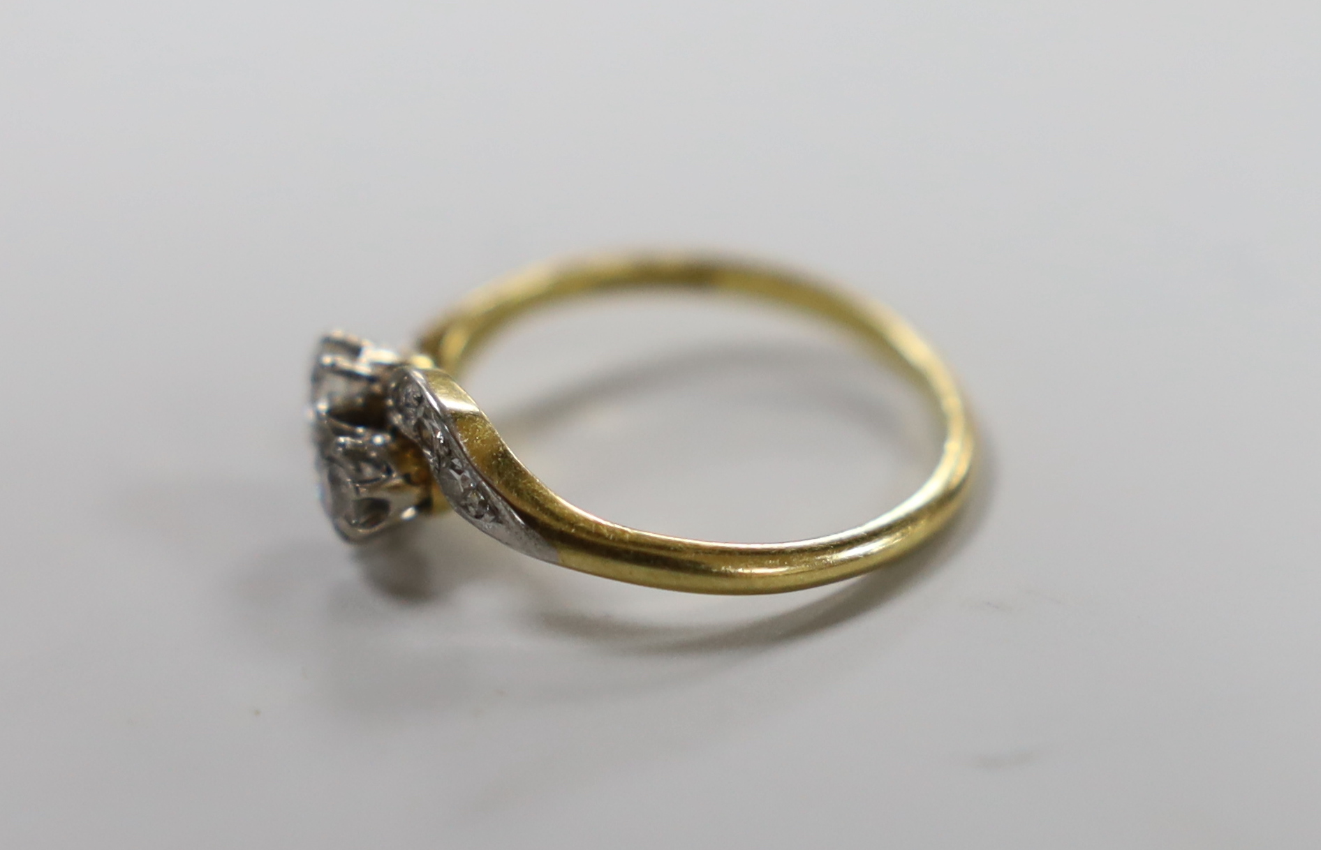 An 18ct, pt and two stone diamond set crossover ring, with diamond chip set shoulders, size P, gross weight 2.8 grams.